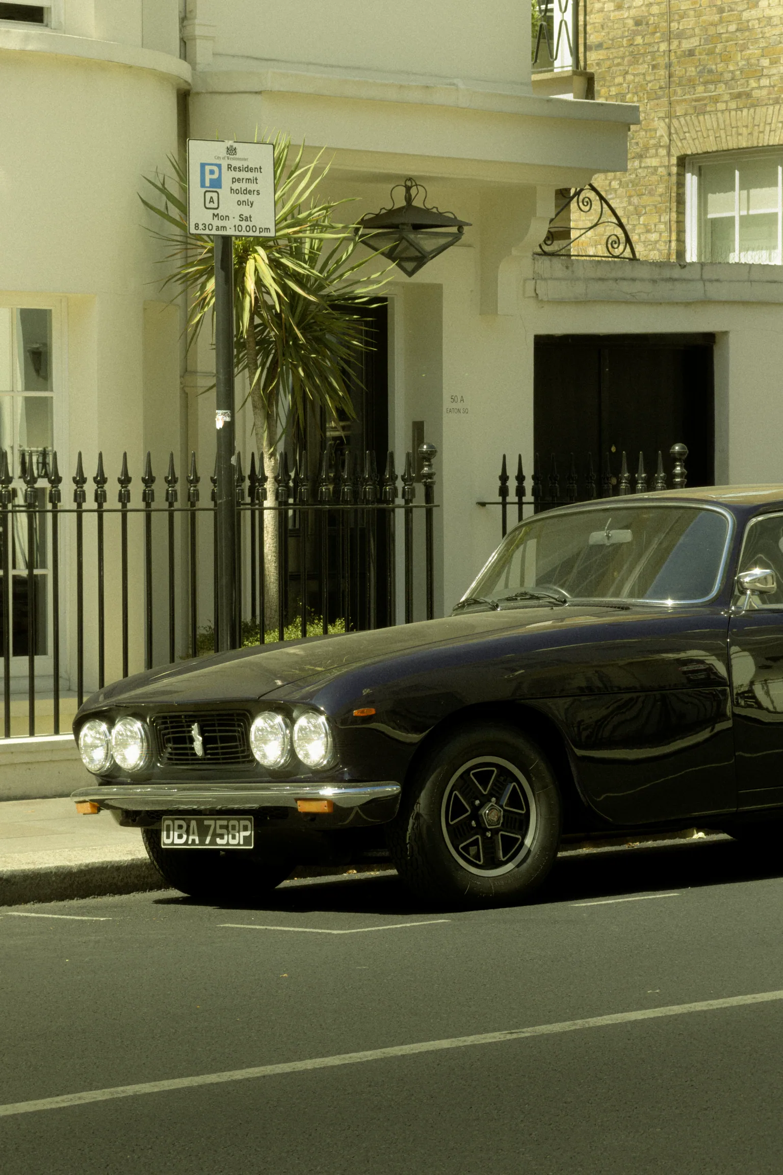 A black Bristol 411 parked outside the white terraced houses of Eaton Square in bright sunlight.