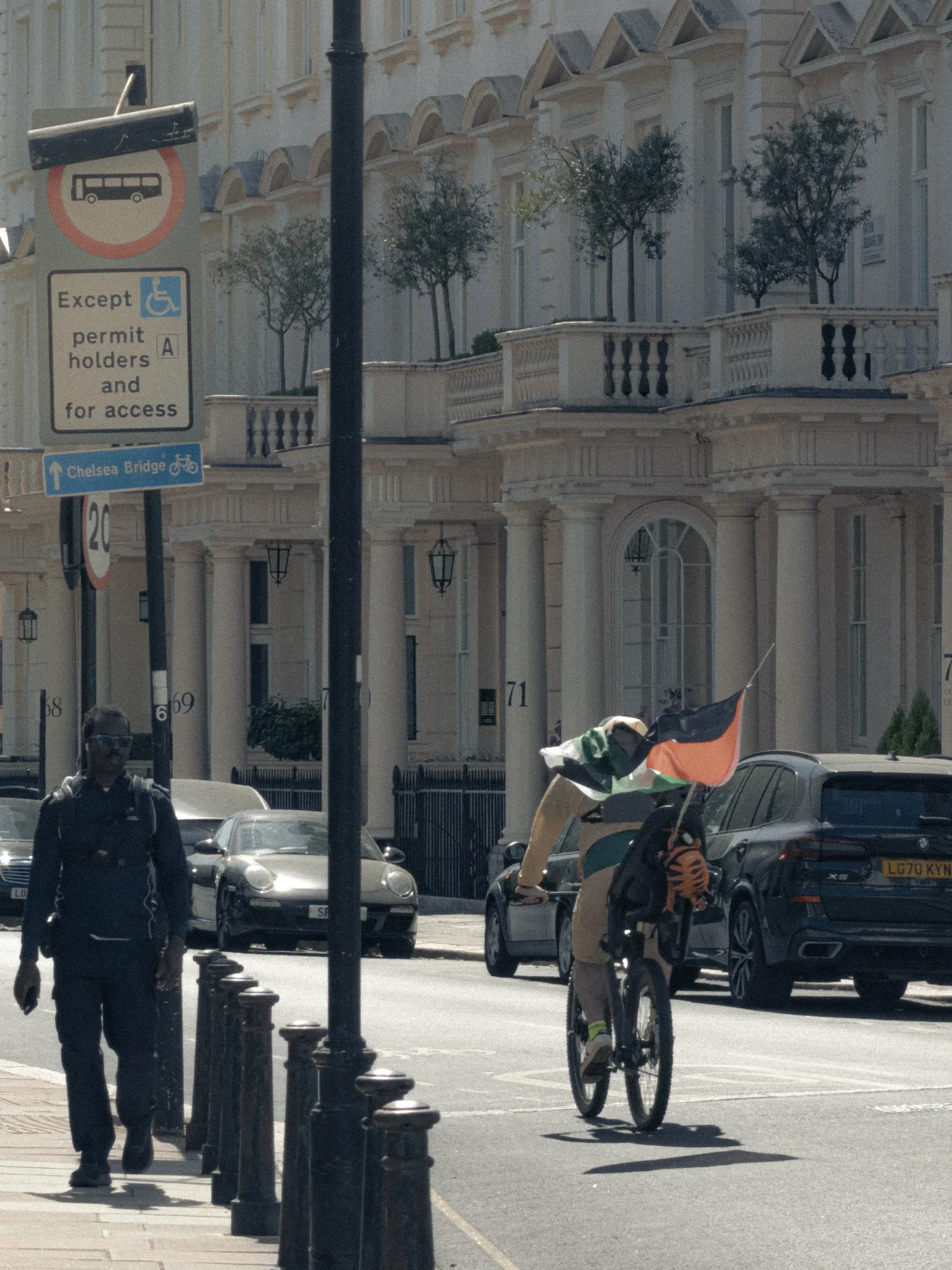 A cyclist carrying a Palestinian flag past the immaculate white façades of Eaton Square.